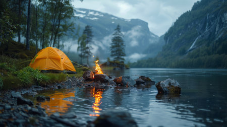 burning fire next to camp tent, near lake or river in mountain valley goes into the distance.の素材