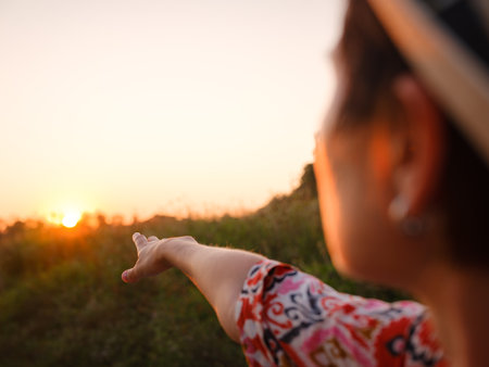 woman gazes at golden sunset over vast countryside, her face illuminated by warm evening glow. Wind gently moves hair as she enjoys peaceful, reflective moment in nature, freedom and serenity.の写真素材