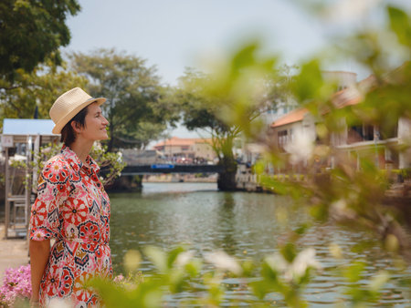 Young woman in ethnic dress and hat exploring the vibrant streets of Malacca, Malaysia. A blend of cultural heritage, colorful architecture, and tropical charm. Perfect travel and lifestyle moments.の写真素材