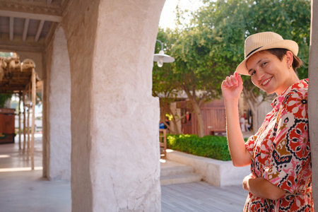 Young woman in an ethnic dress and hat exploring Al Seef Park in Dubai. Surrounded by traditional Emirati architecture and modern vibes, she enjoys the charm of Dubai Creek's cultural heritage.の写真素材