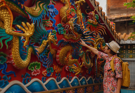 Female hand touches a colorful dragon sculpture on the grounds of a temple in Bangkok. Woman Exploring Colorful Streets Near Buddhist Temples in Bangkokの写真素材