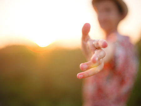 Soft evening light bathes golden field as woman's hand gently moves through tall grass, capturing the sense of freedom, nature, and serenity. Warm sunset hues create a peaceful, dreamy countryside atmosphere.の写真素材