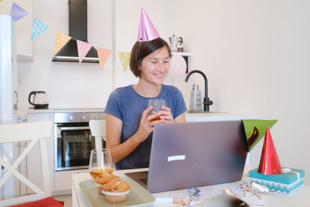 Young woman video chatting with family on her birthday, smiling and joyful as she connects with loved ones from home, celebrating a special day with warmth and connection