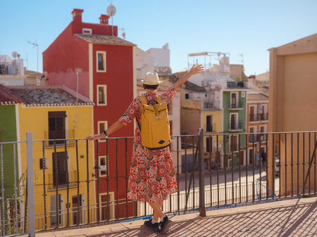 Woman in dress strolls through colorful streets of Spanish coastal town of La Vila Joiosa. sunny winter highlights atmosphere charm of Mediterranean architecture and quiet seaside life, back viewの写真素材