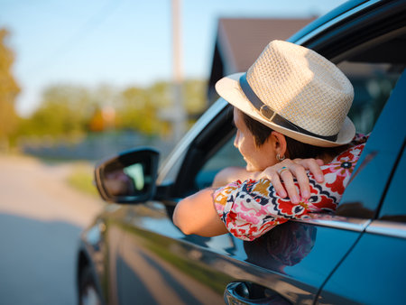 Traveler woman in red ethnic dress and hat drives car through scenic countryside of Croatia in summer. Surrounded by lush fields and forests, she enjoys peaceful and adventurous road tripの写真素材