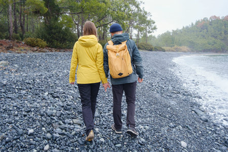 Couple enjoys Turkish coastline. Sitting on stones, watching sea waves, relaxing together, slow romantic moment near calm blue water under soft winter light.の写真素材