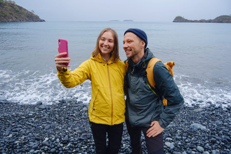 Couple enjoys Turkish coastline and taking selfie on beach in Winter. walking on stones, watching...