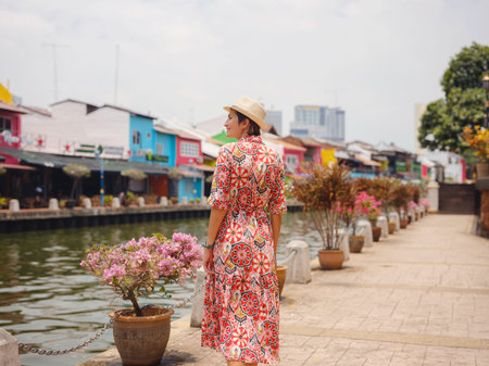 Young woman in ethnic dress and hat exploring the vibrant streets of Malacca, Malaysia. A blend of...