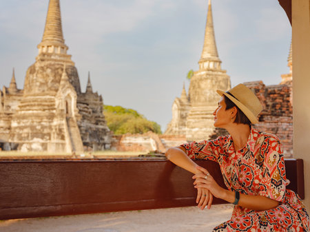 Young female tourist in dress exploring historic park of Ayutthaya, Thailand. Wat Phra Si Sanphet ancient temples and statues, she enjoys peaceful atmosphere and rich cultural heritage.の写真素材