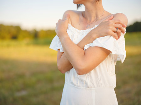 Beautiful woman in white dress standing in summer field during golden sunset in Croatia, warm sunlight, romantic evening mood, natural countryside atmosphere, soft wind and peaceful sceneの写真素材
