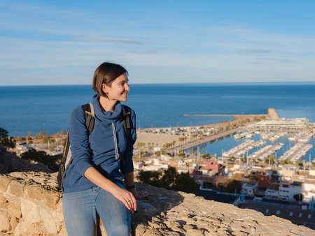 Young woman exploring historic castle in Denia, Alicante province, Spain, scenic views of town below, set against cooler season backdrop. blend of history and tranquility in timeless setting.の写真素材