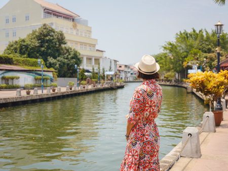 Young woman in ethnic dress and hat exploring the vibrant streets of Malacca, Malaysia. A blend of cultural heritage, colorful architecture, and tropical charm. Perfect travel and lifestyle moments.の写真素材