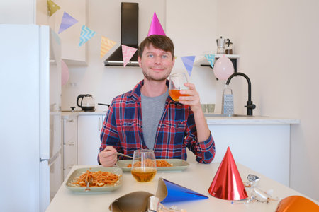 Young man celebrates his birthday at home, surrounded by a cozy and festive setting. He enjoys his...