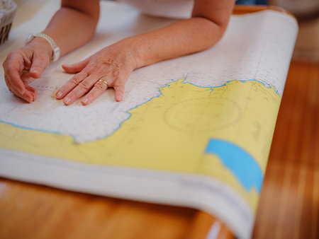 Mature woman sits inside yacht cabin analyzing paper sea chart for route planning. Navigation...