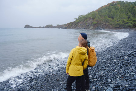 Couple enjoys the coastline. Sitting on stones, watching sea waves, relaxing together, slow romantic...