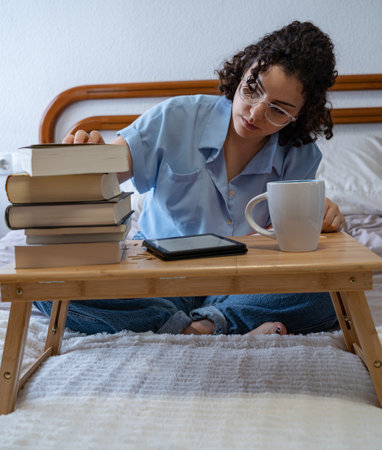 Woman choosing between a book or an e-book while sitting on bedの写真素材