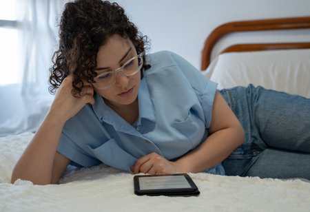 Beautiful woman reads an E-Book lying on her side on bedの写真素材