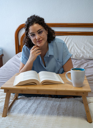 Woman looks at camera while reading a book on bedの写真素材