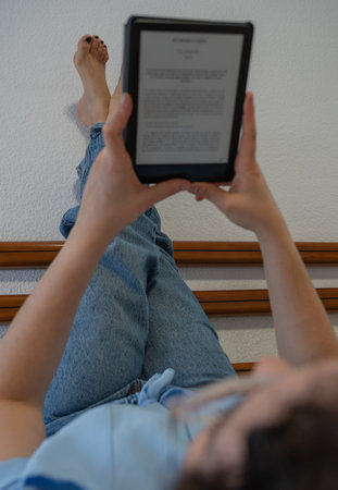 Woman reads an E-Book lying face up on bedの写真素材