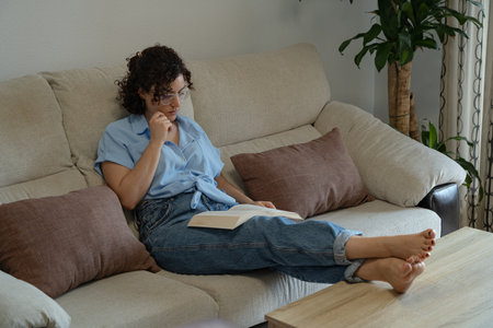 Woman reading a book in the living room with her feet on the tableの写真素材