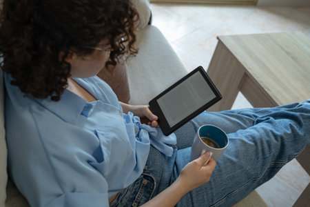 Woman reading an e-book in the living roomの写真素材