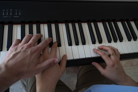 hands of woman playing the piano with other hand of a man in the sceneの写真素材