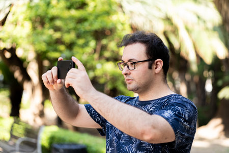Young man with glasses taking photos with his mobile phoneの写真素材