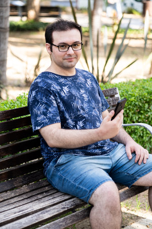 Young man with glasses looking at camera with phone in his handsの写真素材