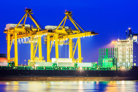 Container Cargo freight ship with working crane bridge in shipyard at twilight