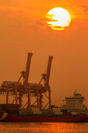 Container Cargo freight ship with working crane bridge in shipyard at sunsetの写真素材