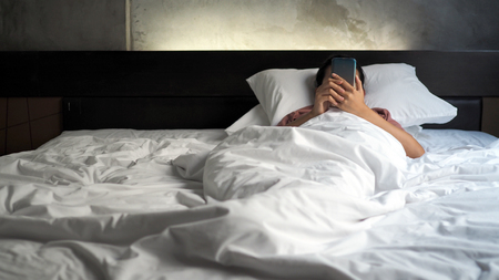 Asian women are using the smart phone on the bed. Mobile addict concept.の写真素材