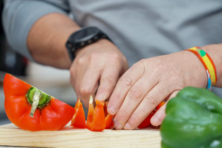 Hands of a man cutting red and green bell pepper on a wooden boardの写真素材