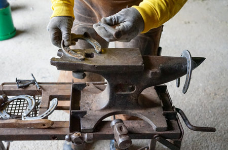 a person's hands with gloves, prepares a horseshoe on an anvil, to shoe his horseの写真素材