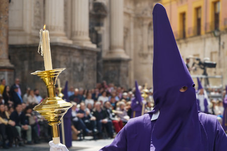 Nazarene in the procession of Good Friday morning, with a candle and a lit candle