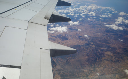The wing of an airplane flies above some clouds and the land and coast of an island, with the rest of the sky and the blue sea, on a summer dayの写真素材