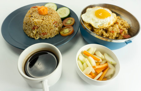Fried rice served with fresh tomatoes and meatballs in a green tosca ceramic plate and pickles on a white bowl on a white backgroundの写真素材