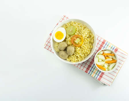 Warm noodles served with fresh tomatoes and meatballs on a white round bowl and pickles on a white bowl on a white backgroundの写真素材