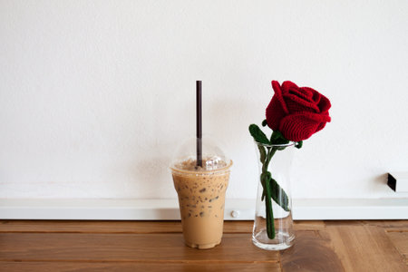 coffee in plastic cup and artificial rose on wooden table over white grunge backgroundの写真素材