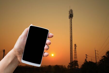 hand hold smart phone on image of Silhouette communication tower in a wonderful sunriseの写真素材