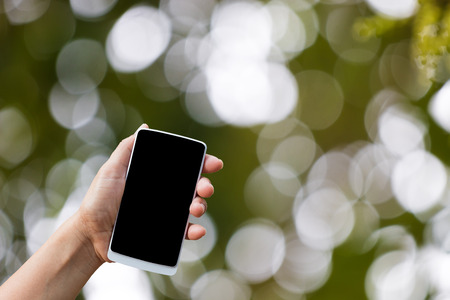 hand hold smart phone,cell phone,mobile over blurred image of green backgroundの写真素材