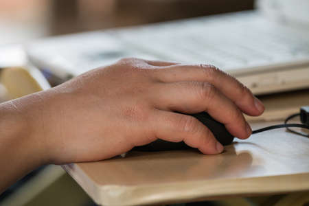 Male hand holding computer mouse with laptop keyboard in the backgroundの写真素材