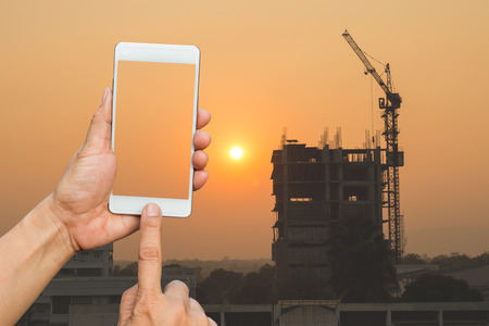 business hand hold smart phone,mobile,cell phone over blurred image of crane buildingの写真素材