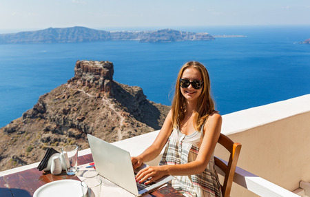 Young woman working at a computer sitting in a cafe on the seafront.の写真素材
