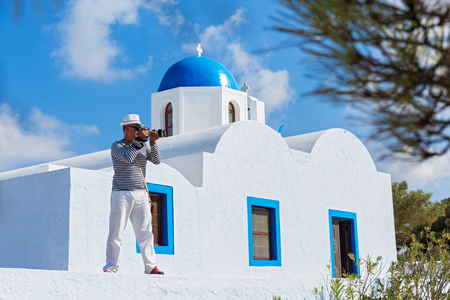 Male photographer in the background of the white Church and architecture of Santorini.の写真素材