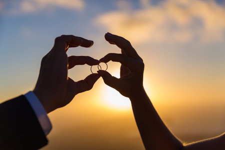Hands and rings the newlyweds on the background of a Golden sunsetの写真素材