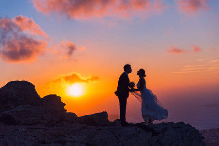 Silhouette of bride and groom on a high rock on a background of sea sunsetの写真素材
