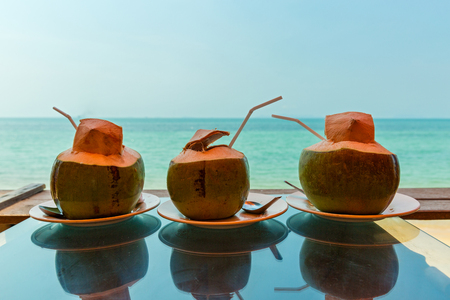 Three coconuts with fresh juice on the table over sea backgroundの写真素材