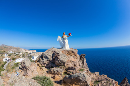 Beautiful woman in white dress stands on a high cliff near the seaの写真素材