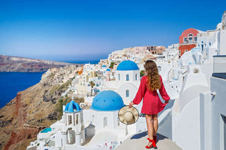 Beautiful, young woman on the roof of the Santorini island building looks at the landscapeの写真素材