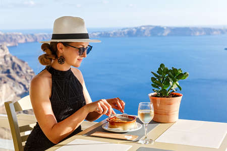 Young woman has dinner in a restaurant overlooking the sea and the island of Santorini, Greeceの写真素材
